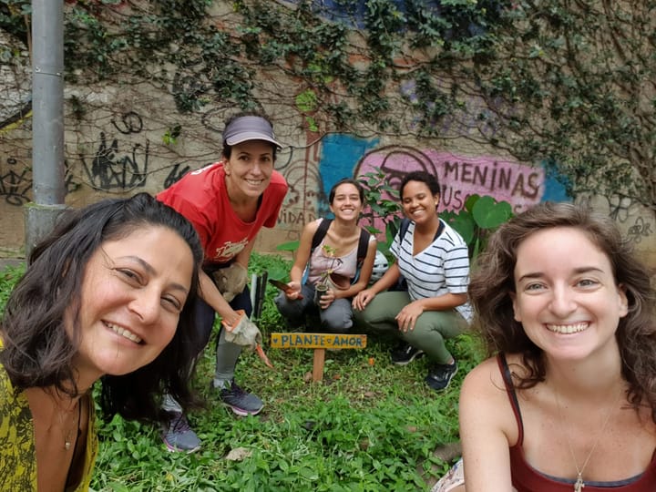 A group of people in the garden surrounding the plants and a wooden sign "plant love"