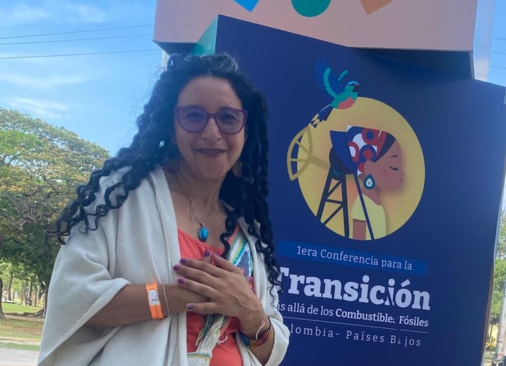 Dennise smiling with hands on heart, next to a Conference poster 